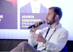 A man speaks into a microphone at a conference, with a nameplate behind him reading 'ASHWIN RAMASWANI, CTO & Co-Founder'.