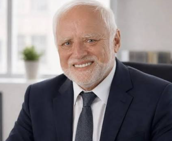 A portrait photograph of an older gentleman with white hair and a beard, wearing a dark blue suit and tie, smiling warmly in what looks like a corporate office setting.