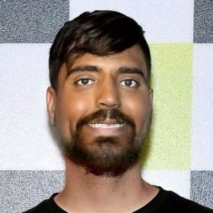 A smiling man with dark hair, a beard, and a mustache poses in front of a checkered gray and yellow backdrop. Given the post's playful "wrong answers only" prompt, responses could humorously misidentify him as anyone from a celebrity lookalike to a famous historical figure.