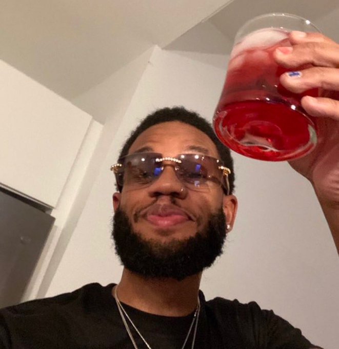 A bearded man wearing designer sunglasses with blue lens reflections raises a glass filled with a red beverage and ice in a celebratory toast, pairing perfectly with the post's excitement about NFT earnings and anticipating the next profitable project.