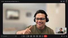 A man wearing glasses and headphones gives a thumbs-up during what appears to be a video call, with a blurred background.
