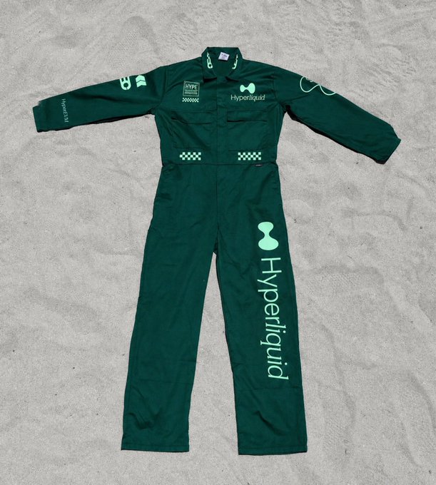 A green Hyperliquid-branded racing suit laid flat on concrete, featuring HYPE logo, checkered flag details, and "Hyperliquid" text printed vertically.