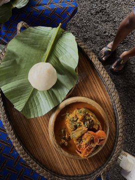 A traditional Nigerian meal of pounded yam and fisherman soup is served on a banana leaf atop a wooden tray, presented as the perfect start to a vacation in Uyo at the #SolanaSummitNigeria 2026.
