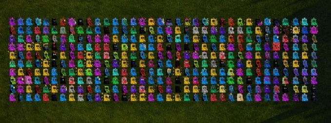An aerial view of a large grid of colorful, hooded digital characters or avatars arranged neatly on a green field.