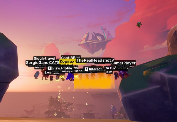 The image shows a colorful, dreamlike virtual landscape with floating islands, a vibrant sunset sky, and a cluster of cartoonish avatars gathered together, displaying usernames such as "SergioGans CATS," "Gigalvltravel," "TheRealHeadshot," "LamerPlayer," "CapitanBBJ," and "kopirax." This aligns with the post about a virtual event hosted by @CryptoCatsApe alongside @kopirax_blog, showcasing the avatars of attendees enjoying the gathering in this imaginative digital environment.