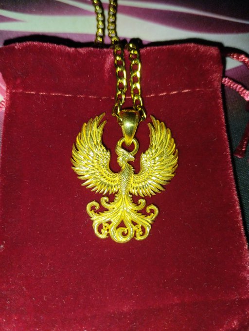 A gold phoenix pendant on a chain rests inside a red velvet jewelry box. The rising bird imagery visually echoes the post's "FEEL THE RISE" message, symbolizing the rebirth and ascent associated with the $METAL (Metal Dollar / XMD) blockchain token.