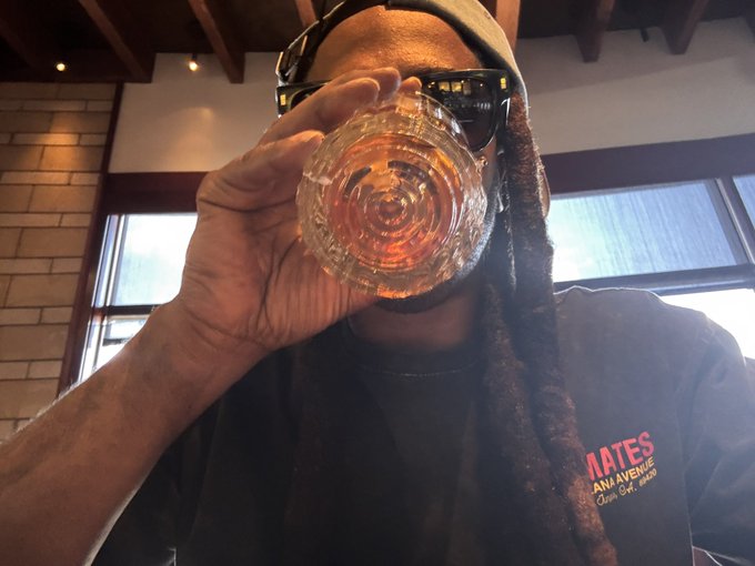 A person wearing sunglasses and a hooded towel drinks from a glass in what appears to be a restaurant or bar setting.