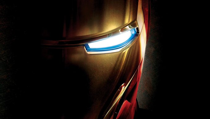 A close-up dramatic shot of Iron Man's helmet with the glowing white eye piece illuminated against a dark background.