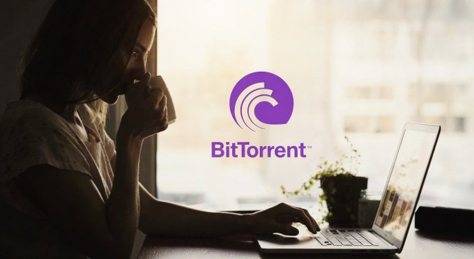 A woman works on her laptop by a window while the BitTorrent logo is displayed prominently in the center, visually reinforcing the message of decentralized, community-powered file sharing where every connected user contributes to the network's strength.