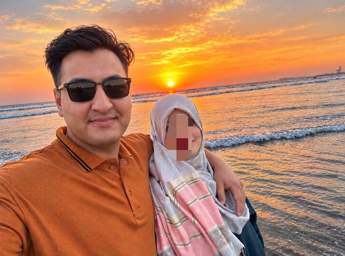 A man wearing an orange shirt and sunglasses takes a selfie at the beach during a vibrant sunset with a woman beside him whose face is blurred. The serene, reflective beach scene mirrors the post's message of perseverance through crypto trading losses, illustrating that calm confidence come after weathering the storms of early mistakes.