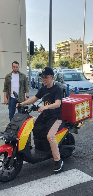A young delivery rider sits on a Meituan (美团) branded electric scooter with a red delivery box, while a man stands behind him on a city sidewalk.

The image visually represents the Chinese post's humorous take on a complete speculative cycle—treating the Meituan delivery scooter as the literal "final stop" for traders who get liquidated on Binance's newly launched 10x leveraged Meituan contracts, joking that losing everything on the trade simply means going to work for the very company you bet on.