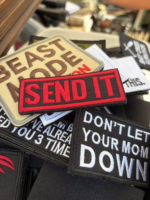A pile of morale patches with bold slogans like "SEND IT," "BEAST MODE," and "DON'T LET YOUR MOM DOWN," displayed alongside what appears to be firearms accessories—evoking the reckless, go-all-in attitude often associated with YOLO-style crypto bets. The image reinforces the post's theme by visually capturing the "send it" mentality that precedes crypto rallies.