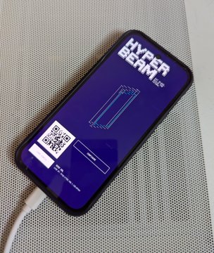 A purple 'Hyper Beam' branded power bank with a built-in cable, a QR code, and what appears to be a digital battery indicator lying on a textured gray surface.