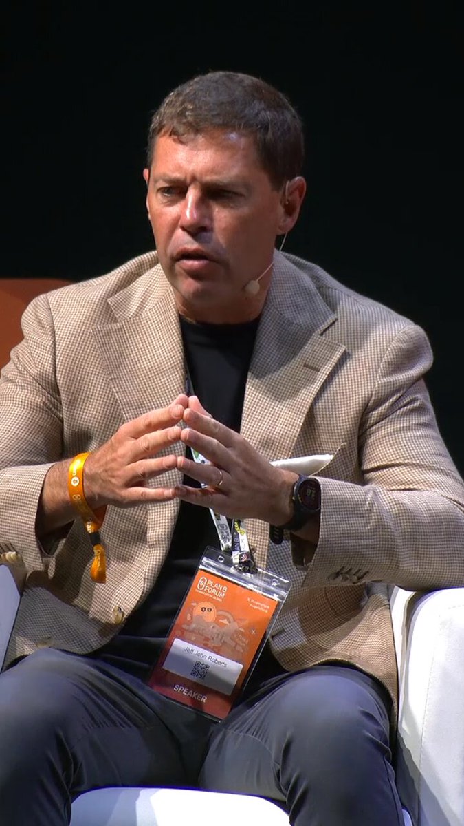 The image shows a man sitting down with his hands clasped together while wearing an orange wristband. He appears to be engaged in a conversation or presentation, possibly at a conference or event. The background of the image is black, which contrasts with the white chair he's sitting on and draws attention to him. The post that accompanies this image discusses the potential inclusion of Bitcoin as part of a country's reserve strategy, suggesting that it could be a valuable asset in uncertain times for some nations.

The man wearing an orange wristband seems to be actively participating in or observing the discussion about Bitcoin reserves. This image captures both the individual and the broader context surrounding the topic at hand.