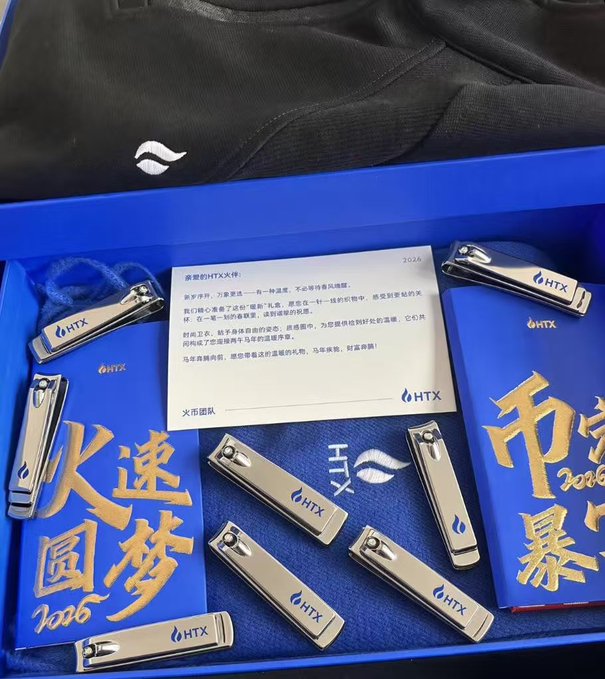 A blue gift box from HTX (火币团队) containing custom branded nail clippers, a 2026 New Year card, and embroidered merchandise with "2026" and Chinese characters (火速圆梦), likely created by a community member responding to an HTX promotional campaign or giveaway.