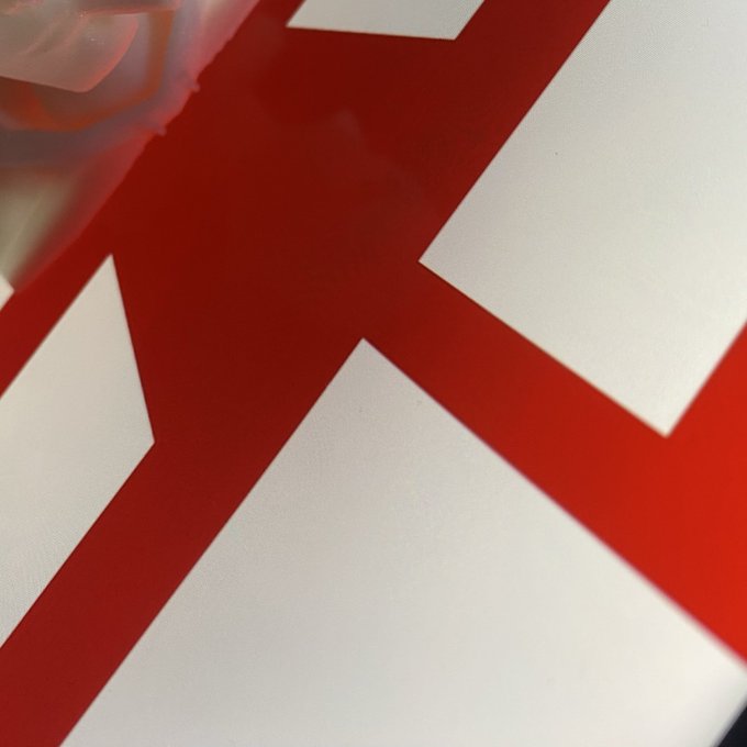 A close-up, partially obscured image of a hand on a large white surface with thick red geometric lines forming a shape.