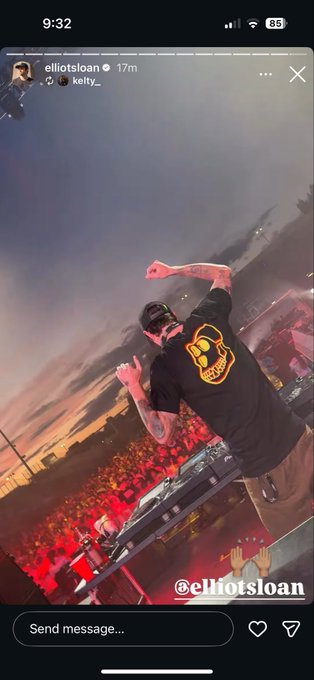 An Instagram story from elliotsloan showing him DJing on stage at sunset with an orange logo t-shirt, tagged with kelly_.