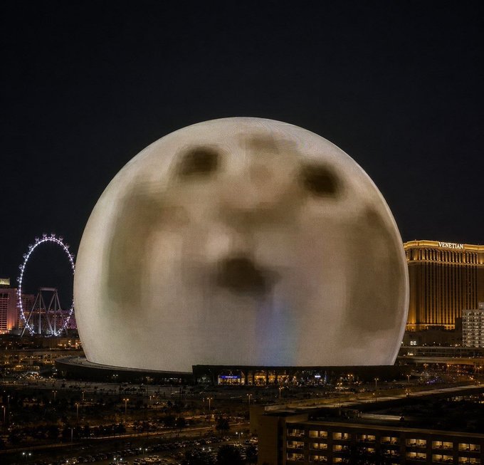 The Las Vegas Sphere at night, humorously edited to resemble a giant shocked or surprised face emoji, with the High Roller observation wheel and Venetian hotel visible in the background.