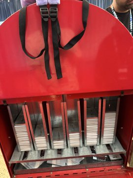 A red metal multi-slot holder contains numerous stacks of small square cards or tiles organized in vertical compartments.