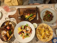A delicious spread of dishes including a grilled meat platter, a creamy corn-topped dish, a colorful salad, stir-fried greens, and bread, shared during a joyful weekend gathering with close friends. The post "周末愉快！和小姐妹的小开心. #美食" (Happy weekend! Small joys with my girlfriends. #Food) perfectly captures the festive and happy atmosphere of the meal.