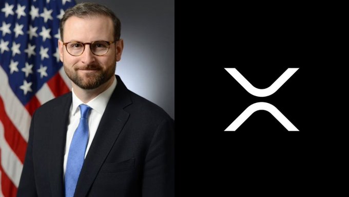 A man in a suit and tie with glasses stands in front of an American flag, positioned next to a black background featuring the white XRP cryptocurrency logo. The image accompanies a post in which the White House Crypto Chief emphasizes Bitcoin's distinction from XRP while forecasting massive capital inflows into the crypto market.