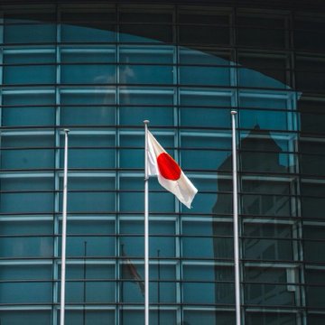 The national flag of Japan waving on a flagpole in front of a modern building with a glass facade.