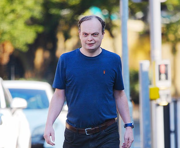A photo of a man in a navy blue t-shirt with a Polo logo and jeans walking on a city street.