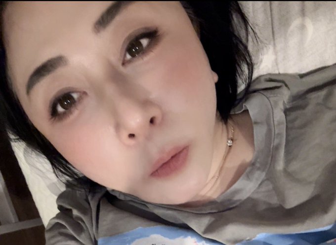 A close-up selfie of a young woman with dark hair, wearing a gray t-shirt and a delicate necklace, looking toward the camera with a soft expression. The post discusses Bitcoin dropping back to the $78K range, suggesting the image likely belongs to a crypto market commentator reacting to the latest price movement and geopolitical tensions affecting crude oil prices.