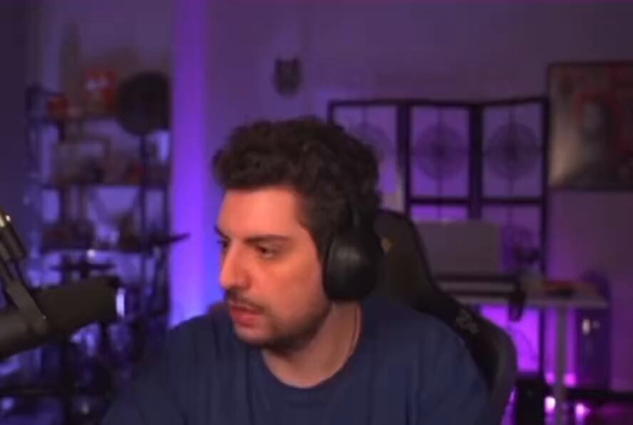 The image features a man wearing headphones sitting at a desk with a microphone attached to his ear. The background of the image shows a purple wall, which could be part of an office or studio setting. There are also several books scattered around the room, suggesting that this space is used for work or study purposes. The caption provided in the image reads "While Bitcoin is dropping right now, let'S remember the legend. We instant #Crypto investors". This message seems to be related to the man's current situation and could possibly be a reference to Bitcoin or cryptocurrency news.