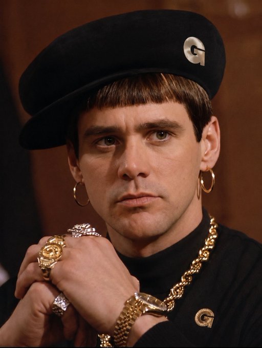 A man wearing a black beret with a gold 'G' pin, gold hoop earrings, multiple gold rings, a gold watch, and a gold chain necklace, with a serious expression.