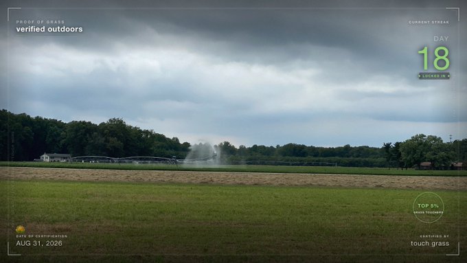 A wide landscape shot of a large grassy field with a sprinkler running under a cloudy sky, featuring overlay text reading 'PROOF OF GRASS verified outdoors', 'DAY 18 LOCKED IN', and 'AUG 31, 2026'.
