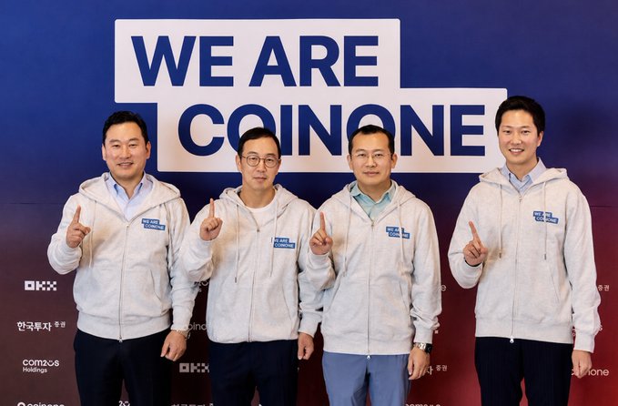Four men in white hoodies pose with pointing gestures in front of a "WE ARE COINONE" backdrop, with logos of OKX and OKX Ventures visible at the bottom, reflecting the recent OKX Ventures acquisition of a 20% stake in the South Korean crypto exchange Coinone.