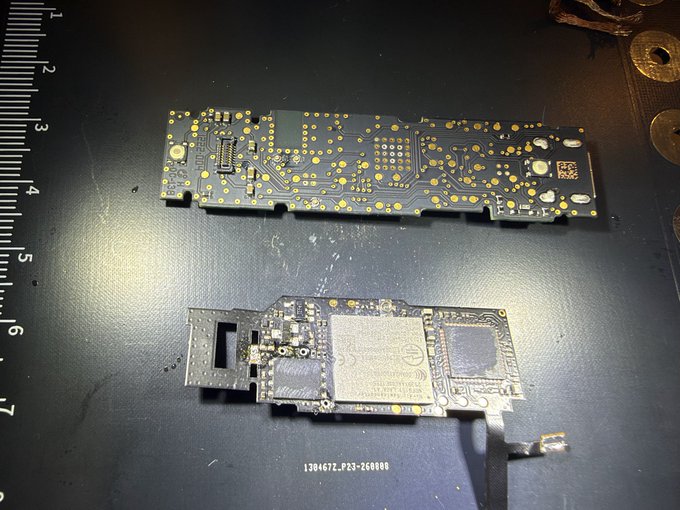 Two disassembled circuit boards are displayed on a dark surface next to a ruler, with the caption "13046272_P33-260898" visible at the bottom. The post suggests the lower board contains a "spy implant" hidden inside a Ledger hardware wallet, while the upper image shows what appears to be an authentic Ledger circuit board for comparison. This image is part of an ongoing scam campaign targeting Ledger users, where fraudsters replace legitimate hardware wallets with tampered devices to steal cryptocurrency recovery phrases.