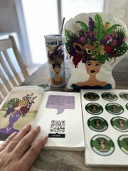 A still life shows a decorative card featuring a deer with flowers for antlers next to a container with matching stickers, with a hand visible on the left side.