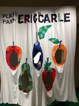 A fabric banner reads 'PLAY PARK ERIGCARLE' with cut-out holes decorated to resemble colorful fruits including apples and a strawberry.