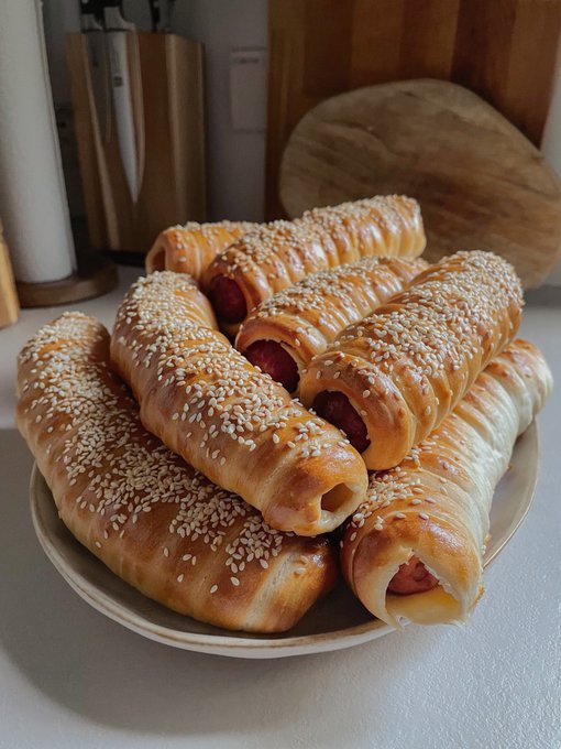 A plate piled high with freshly baked pastry rolls filled with sausage and generously coated with sesame seeds.