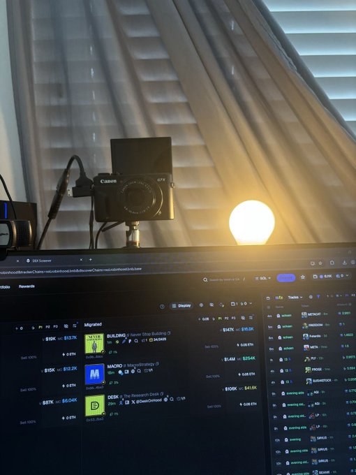 A Canon G7X camera on a tripod is set up above a monitor displaying the pump.fun website with trending tokens, alongside a glowing round light bulb.