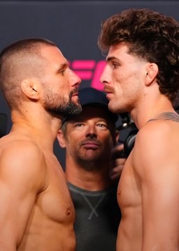 Two shirtless fighters, Mateusz Gamrot and Quillan Salkilld, face off nose-to-nose at what appears to be a UFC weigh-in or pre-fight press event in Las Vegas, with a man in a black cap standing between them against a backdrop featuring UFC branding.