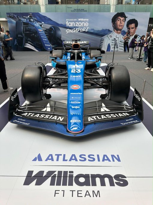 A blue Atlassian Williams F1 Team race car is on display with sponsor logos including Atlassian, Gulf, and Pirelli, with banners in the background reading 'Atlassian Williams Fan Zone Singapore'.