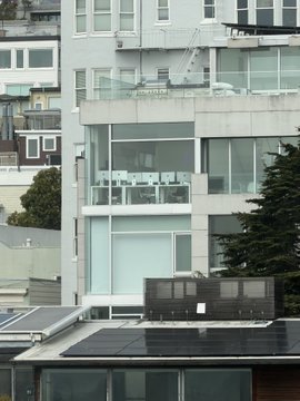 A modern multi-story building in San Francisco with large glass windows, balconies, and rooftop solar panels sits beside a tall tree, illustrating the city's blend of upscale residential architecture and environmental features. The image supports the claim that SF's distinctive, high-quality housing and infrastructure—rather than just its population size—give it outsized cultural and economic influence.
