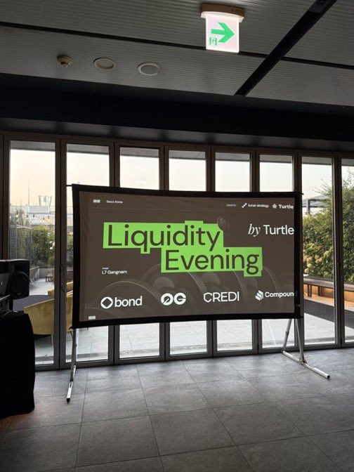 A 'Liquidity Evening by Turtle' event banner displayed in a venue with large windows and an emergency exit sign visible above.