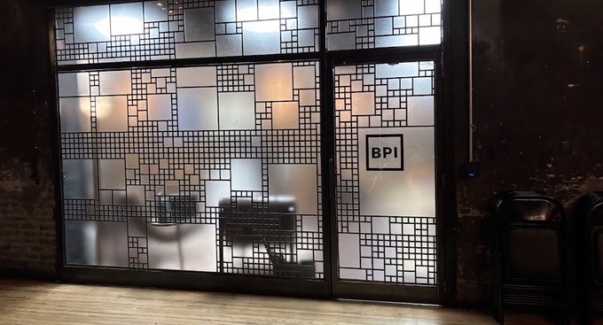 An interior view shows a frosted glass door and window with a geometric grid pattern, displaying a 'BPI' sign, with stacked chairs visible to the side.