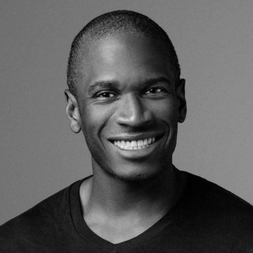 The user wants a caption for the image.
1.  **Analyze the image:** The image is a black and white headshot of a smiling Black man. He has short hair and is wearing a dark t-shirt. The background is a plain, neutral grey.
2.  **Analyze the text provided:** The text says: "Arthur Hayes says Trump has to be the "AI president" first, not the "crypto president," because the entire US economy right now is predicated on AI."
3.  **Identify the person:** The man in the photo is Arthur Hayes, founder of BitMEX. This matches the name in the text.
4.  **Synthesize:** The image shows Arthur Hayes. The text discusses his views on AI and crypto. The caption needs to describe the image concisely.
5.  **Drafting the caption:** "A black and white portrait of Arthur Hayes." Or "Arthur Hayes smiles in a black and white headshot