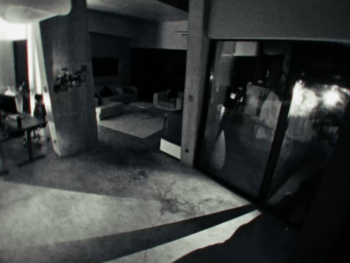 This black and white photograph showcases an empty living room that appears somewhat poorly maintained, with a carpeted floor and several pieces of furniture including couches and chairs scattered throughout the space. The photo was taken from behind a door, making it difficult to see what's on the other side. It seems like someone staged the scene for an article or advertisement, as there are clues suggesting that the room might have been a break-in investigation or involved some form of staged crime.