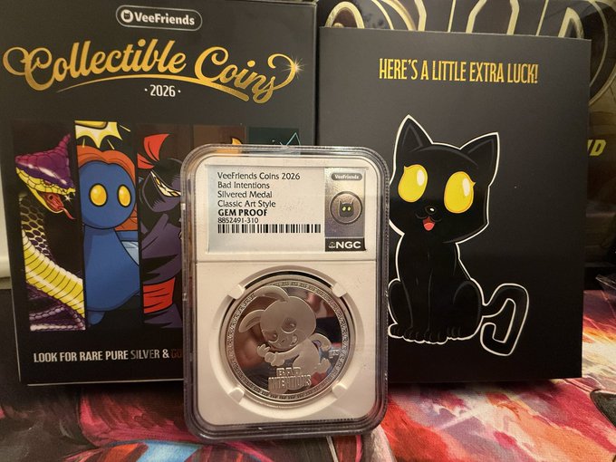 A graded Veefriends 2026 Collectible Coin featuring "Bad Intentions" (Classic Art Style, Silvered Metal, NGC GEM PROOF) sits in its NGC slab in front of the Veefriends Collectible Coins 2026 packaging and a "Here's a Little Extra Luck!" card with a black cat, celebrating a fun unboxing/mail call moment for fans.