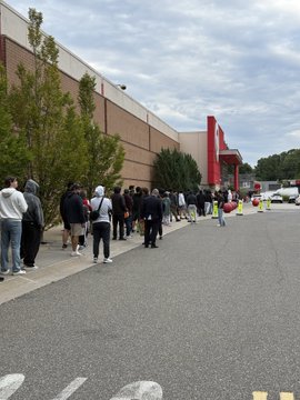 A long line of people stretches outside a Walmart store, with empty pallets visible near the entrance. The scene reflects the post's account of waiting 2.5 hours for the Pokémon 30th Anniversary release, only to find all boxes already emptied by the time they reached the front.