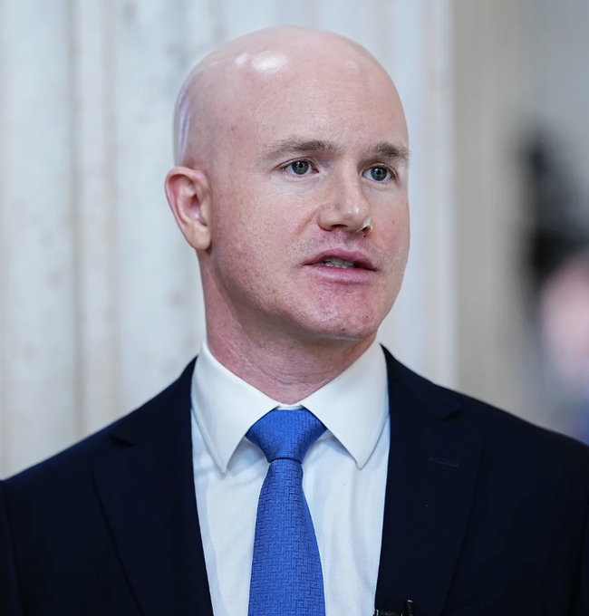 A bald man in a dark suit, white shirt, and blue patterned tie speaks with a serious expression, identified as Coinbase CEO Brian Armstrong reacting to the Senate's failure to advance the Clarity Act, expressing disappointment while maintaining that crypto regulatory clarity will prevail through existing SEC and CFTC frameworks.