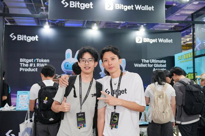 Two men pose for a photo at the Bitget Wallet booth, with branding visible reading "Bitget rToken The #1 RWA Product" and "The Ultimate Wallet for Global Assets."