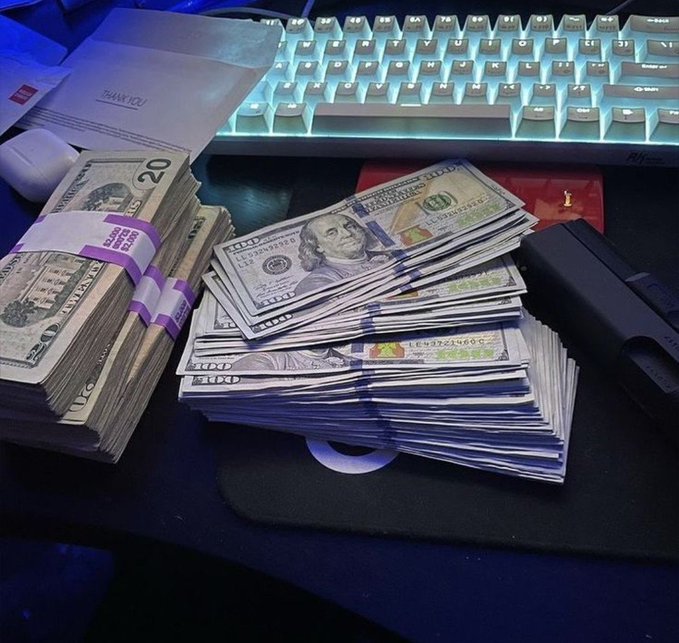 Stacks of $20 bills and a banded bundle of cash sit next to a backlit keyboard and what appears to be a firearm, seemingly used to flaunt wealth in a "$10 giveaway" crypto promotion on social media.