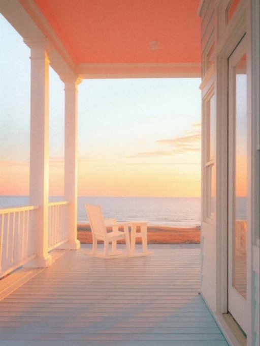 A peaceful view from a porch with a pink ceiling, looking out past a white rocking chair toward a calm ocean during sunset or sunrise.